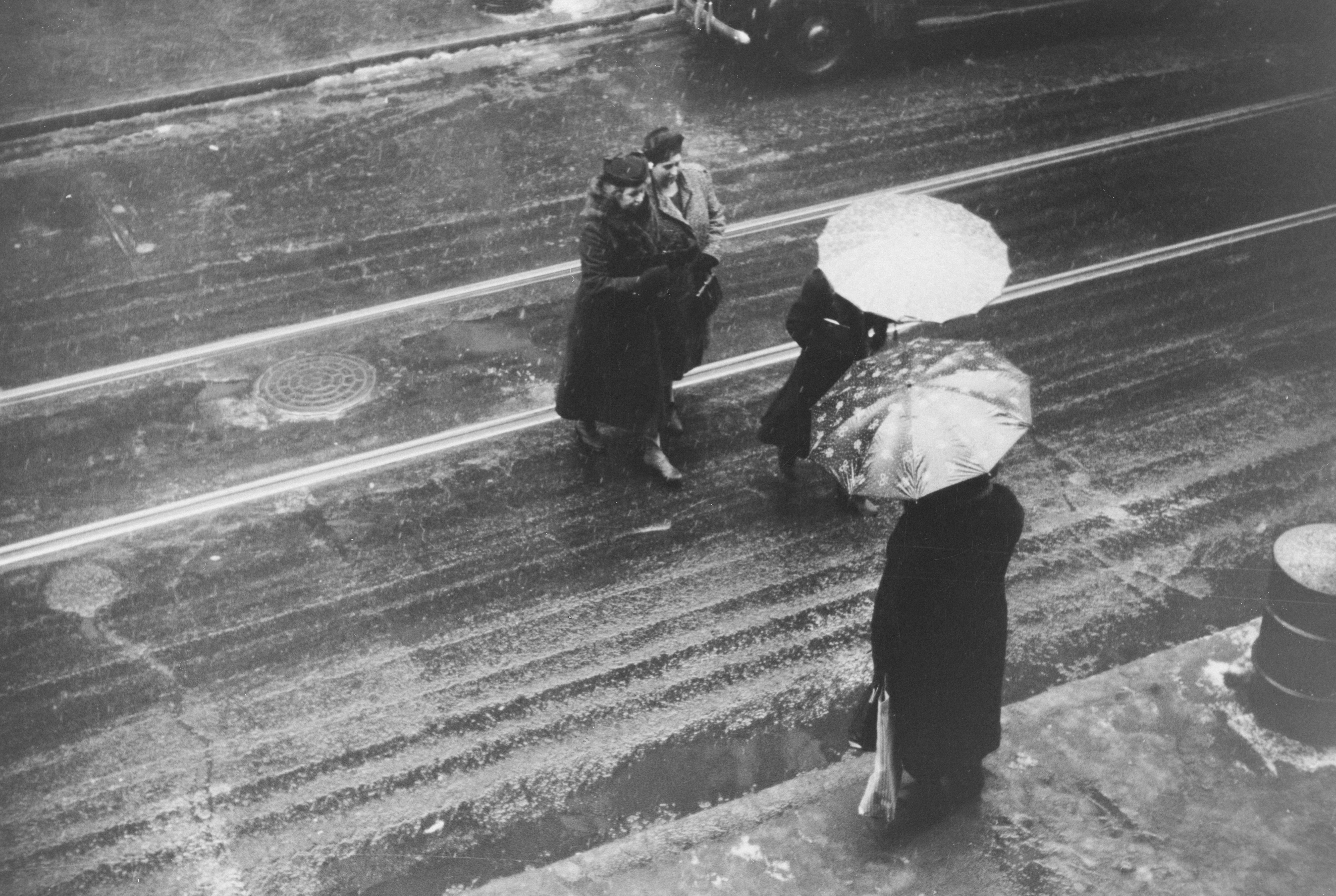 Black and white people with umbrellas on wet tram tracks