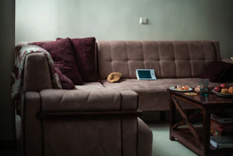 A sectional sofa with pillows and a tablet on it.