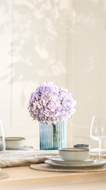 A vase of purple hydrangeas on a table setting.