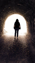 Silhouette of a person walking towards light in a tunnel
