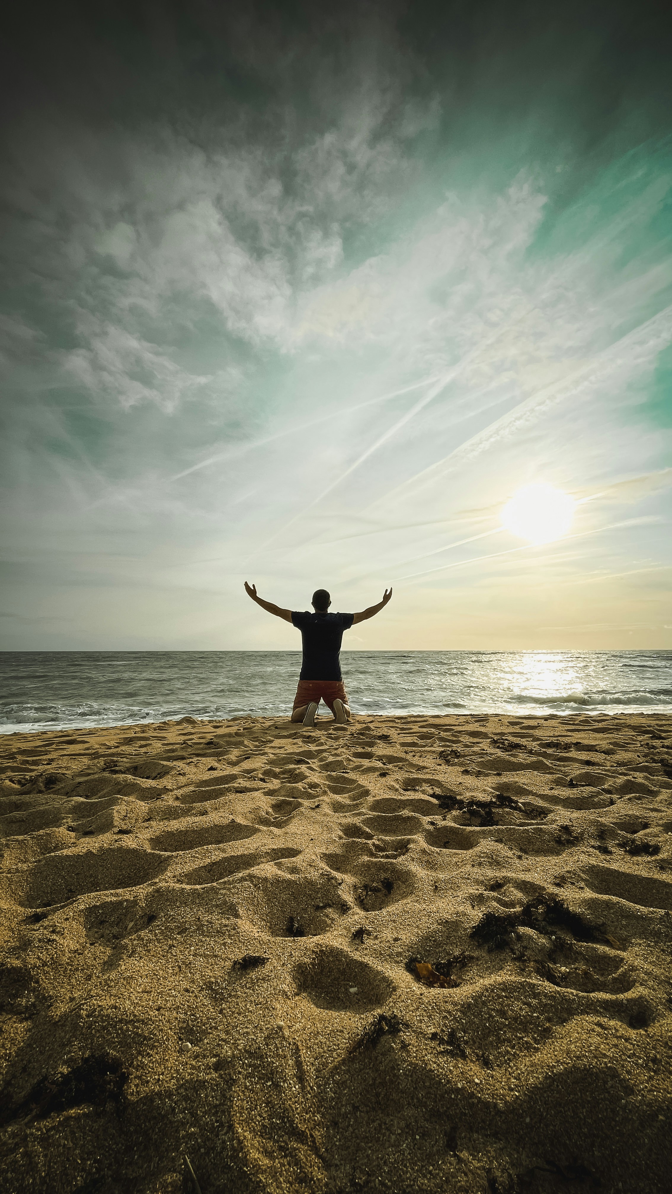 Man with arms raised on beach at sunset