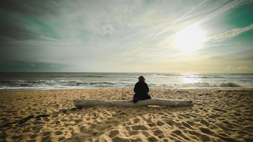 Person sitting on log facing the ocean waves.