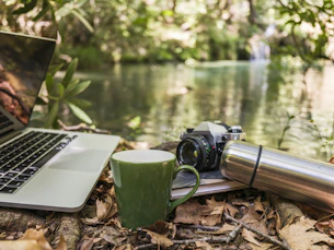 Laptop, camera, and mug by a forest stream