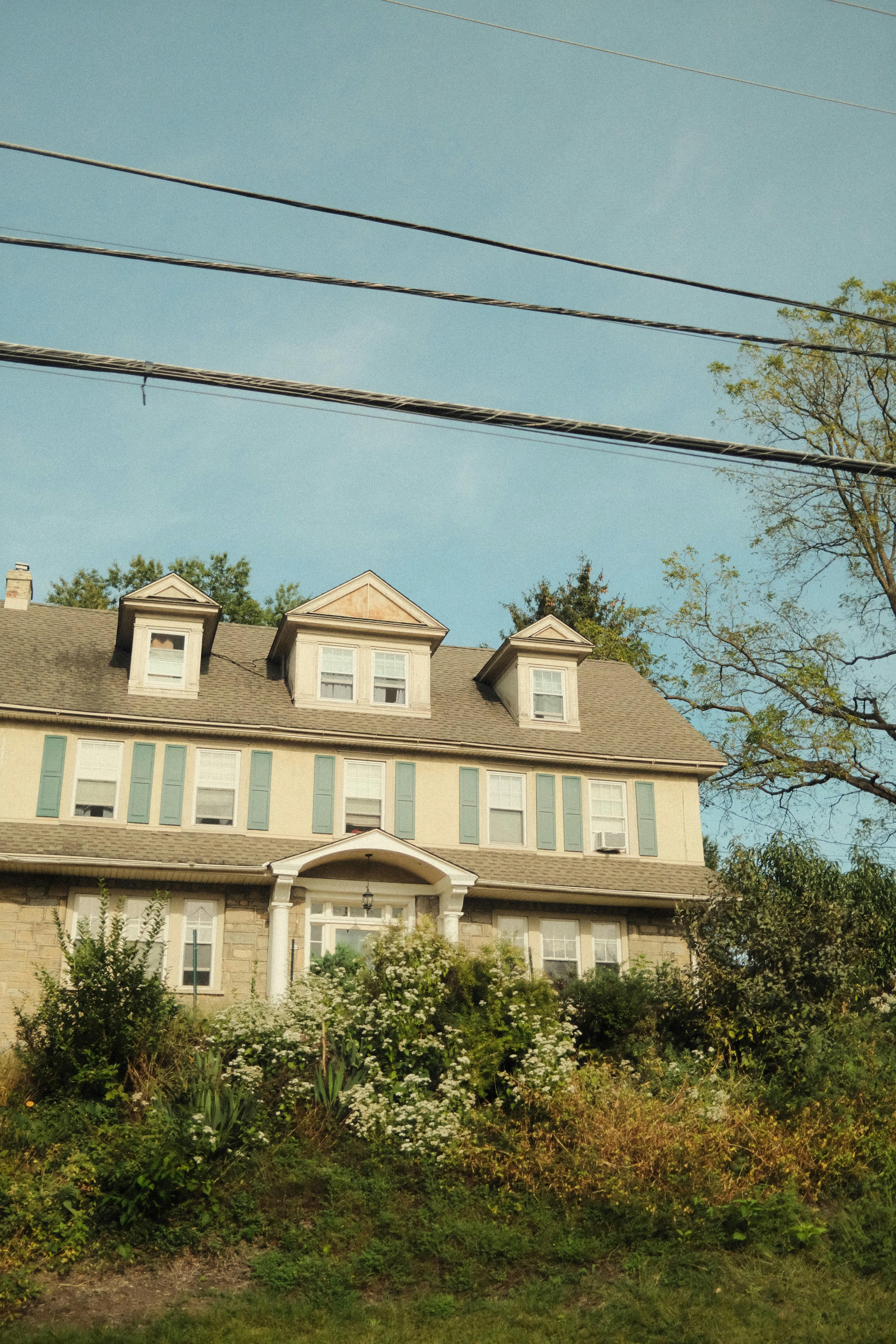 Large house with dormer windows and lush greenery.