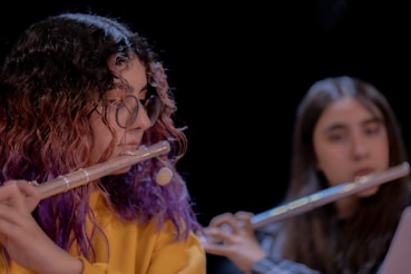 Two girls playing flutes in front of a black background.
