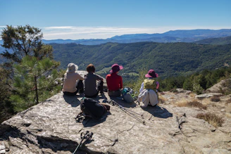 Four people sit on a rocky cliff overlooking a valley.