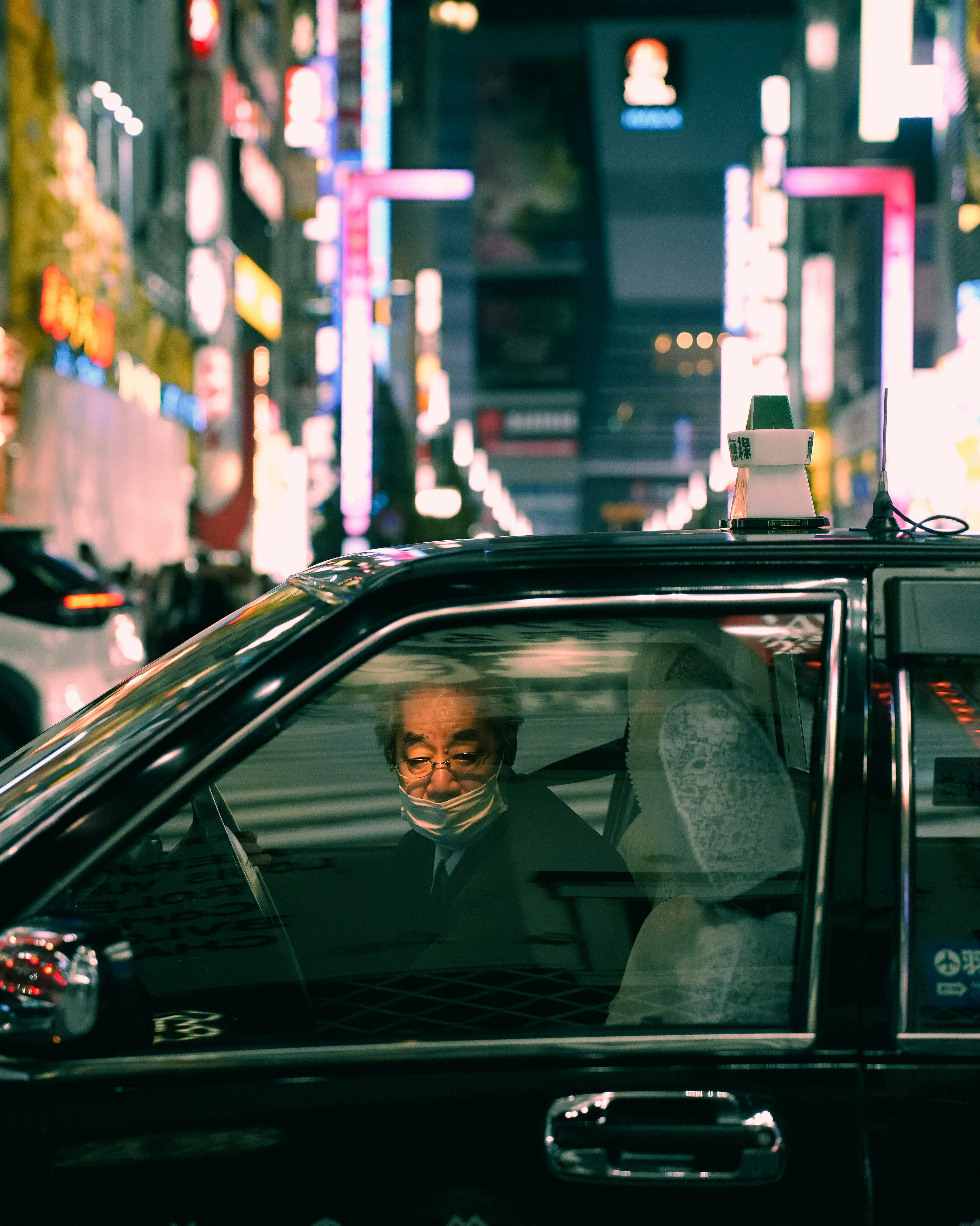 Elderly man drives taxi through neon city street.