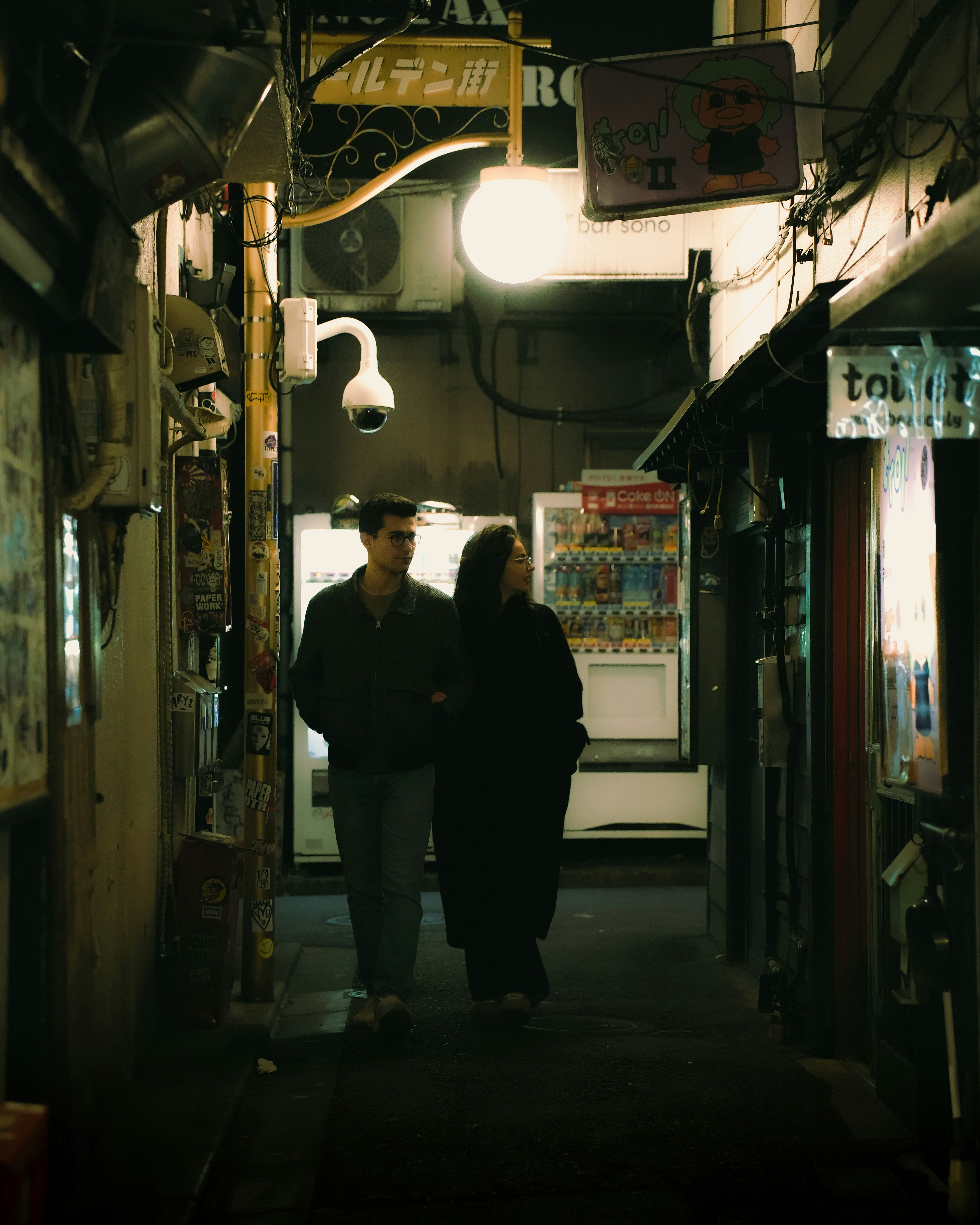 Couple walking down a narrow, dimly lit alleyway at night.