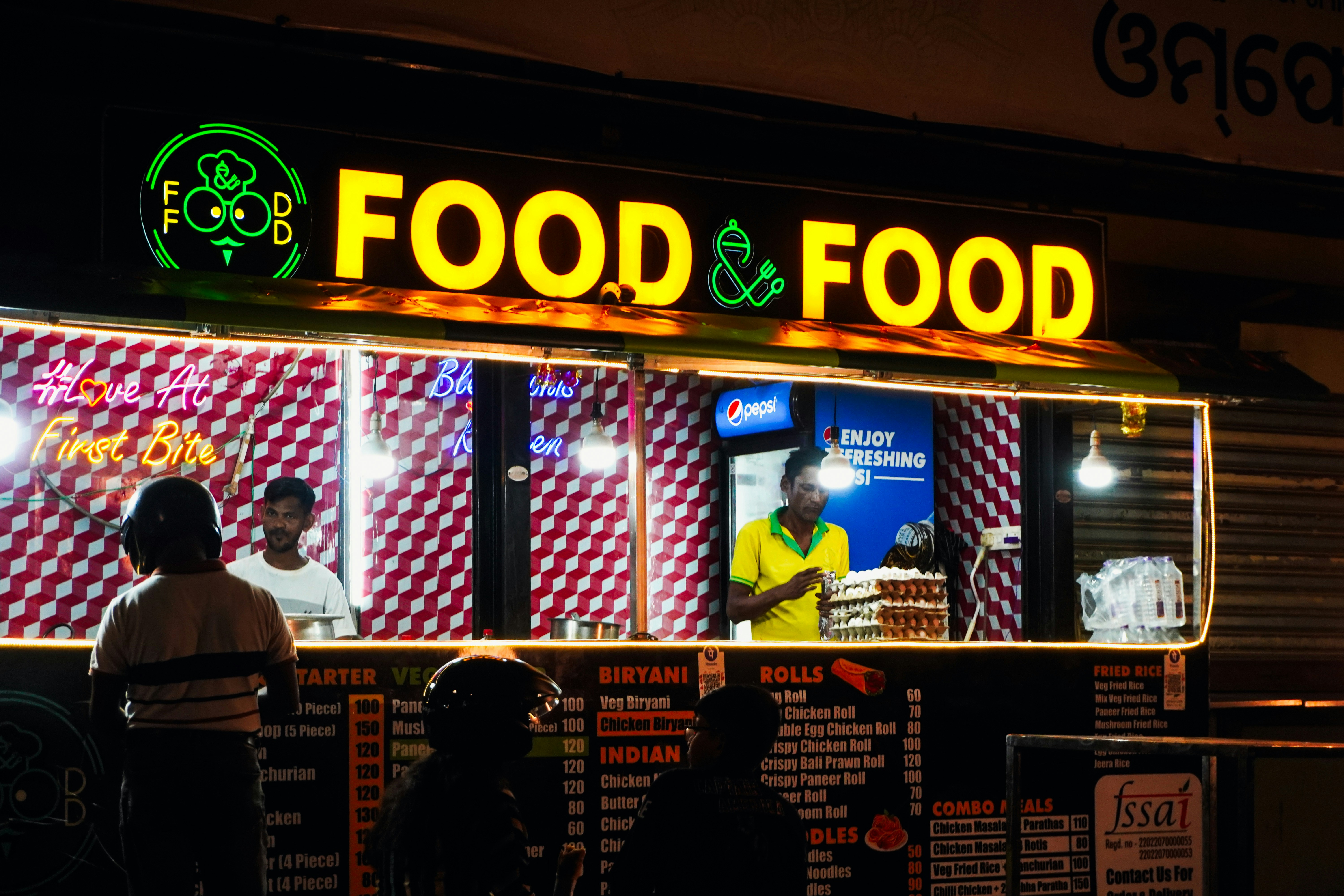 Food stall with bright "food & food" sign at night.