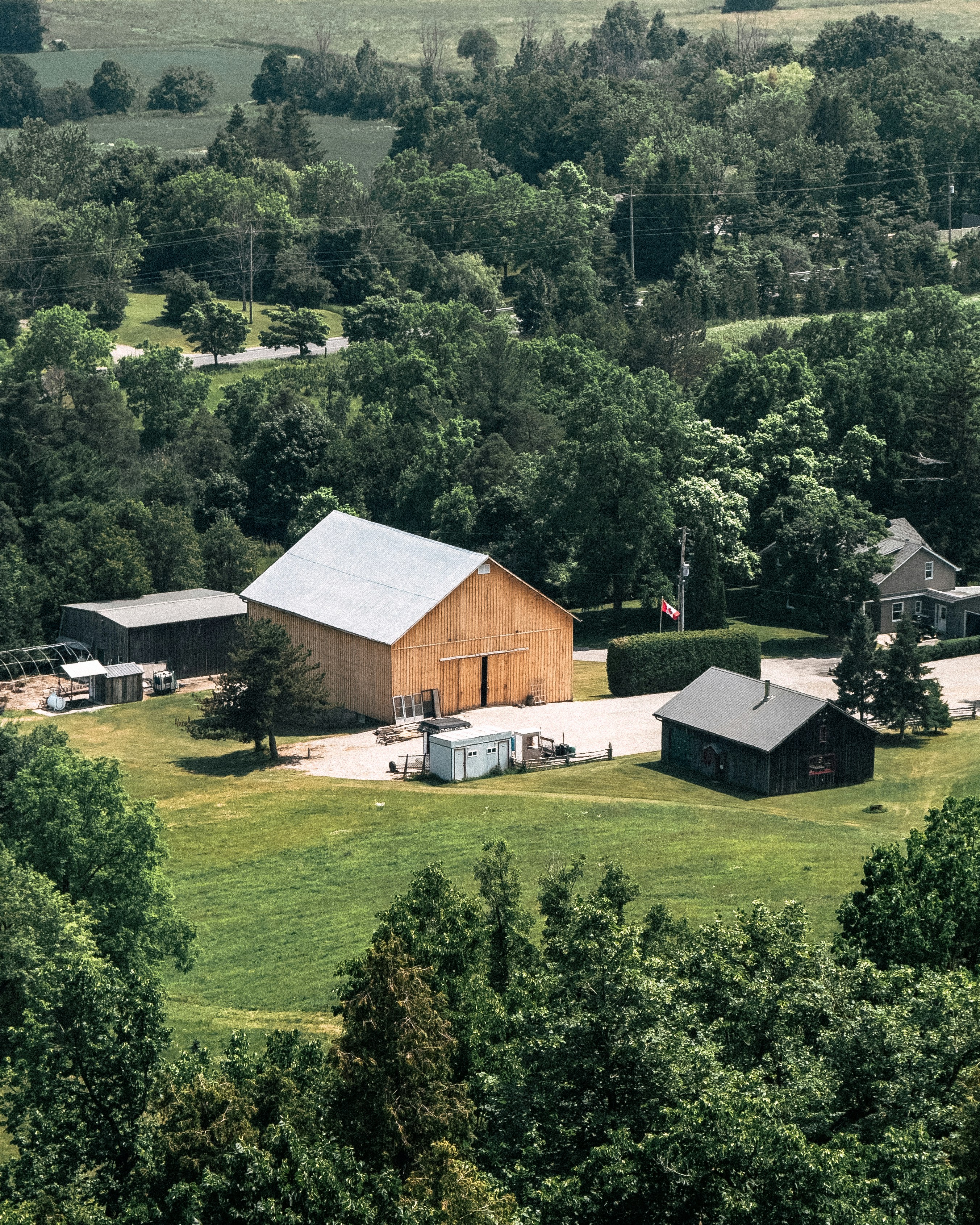 Wooden barn and buildings in a green, tree-filled landscape.