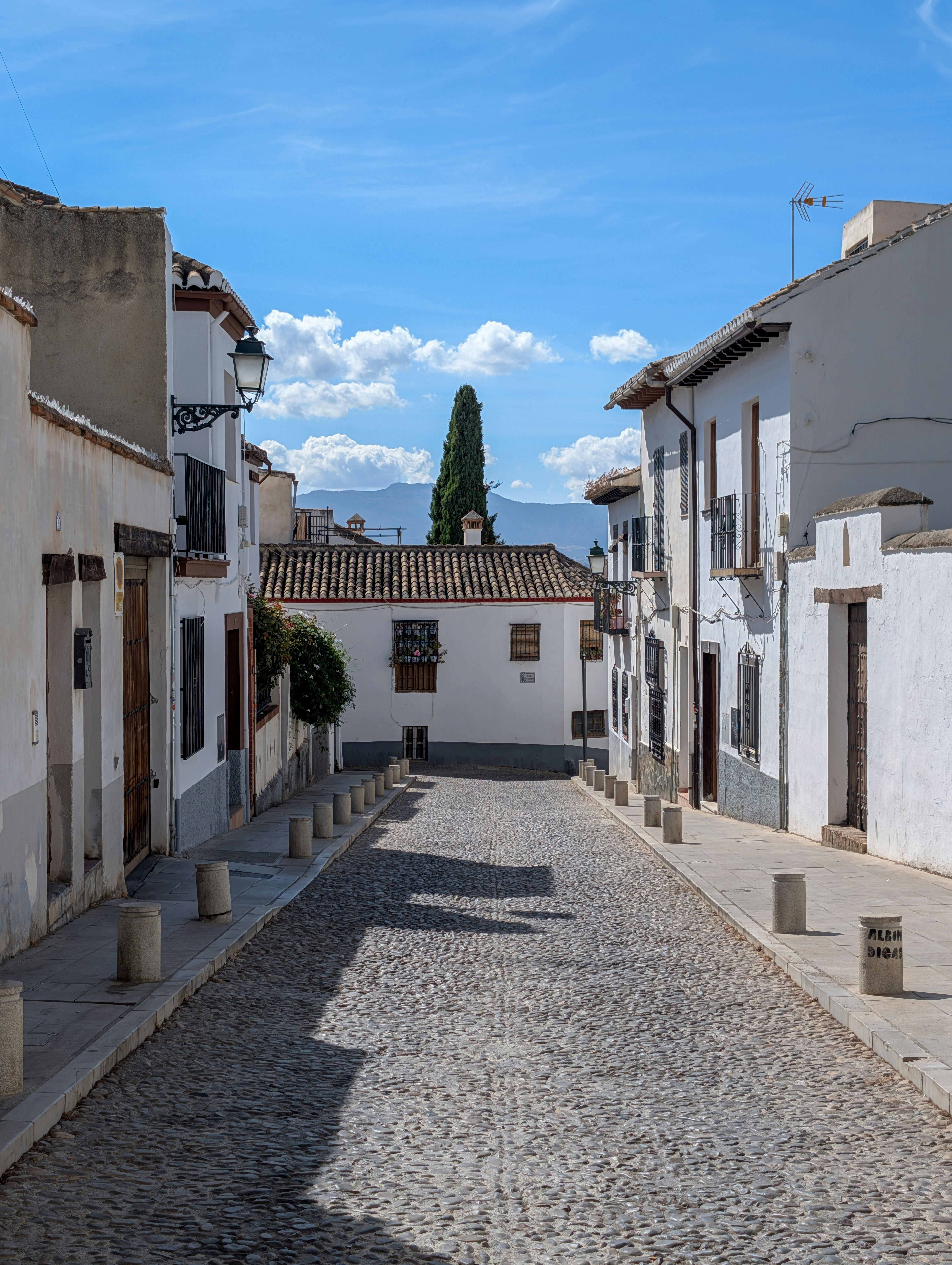 Cobblestone street lined with white buildings under blue sky