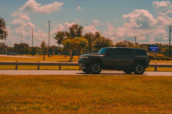 Dark suv drives along a grassy roadside.