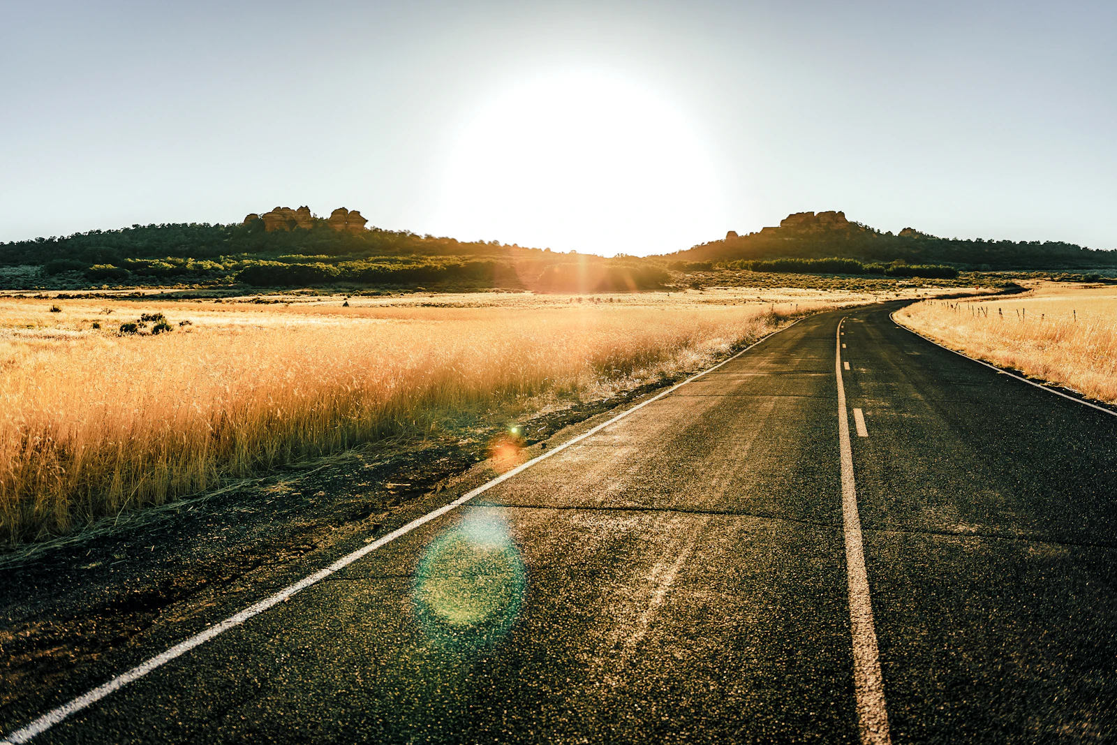 An open road leading toward sunlit hills at sunrise