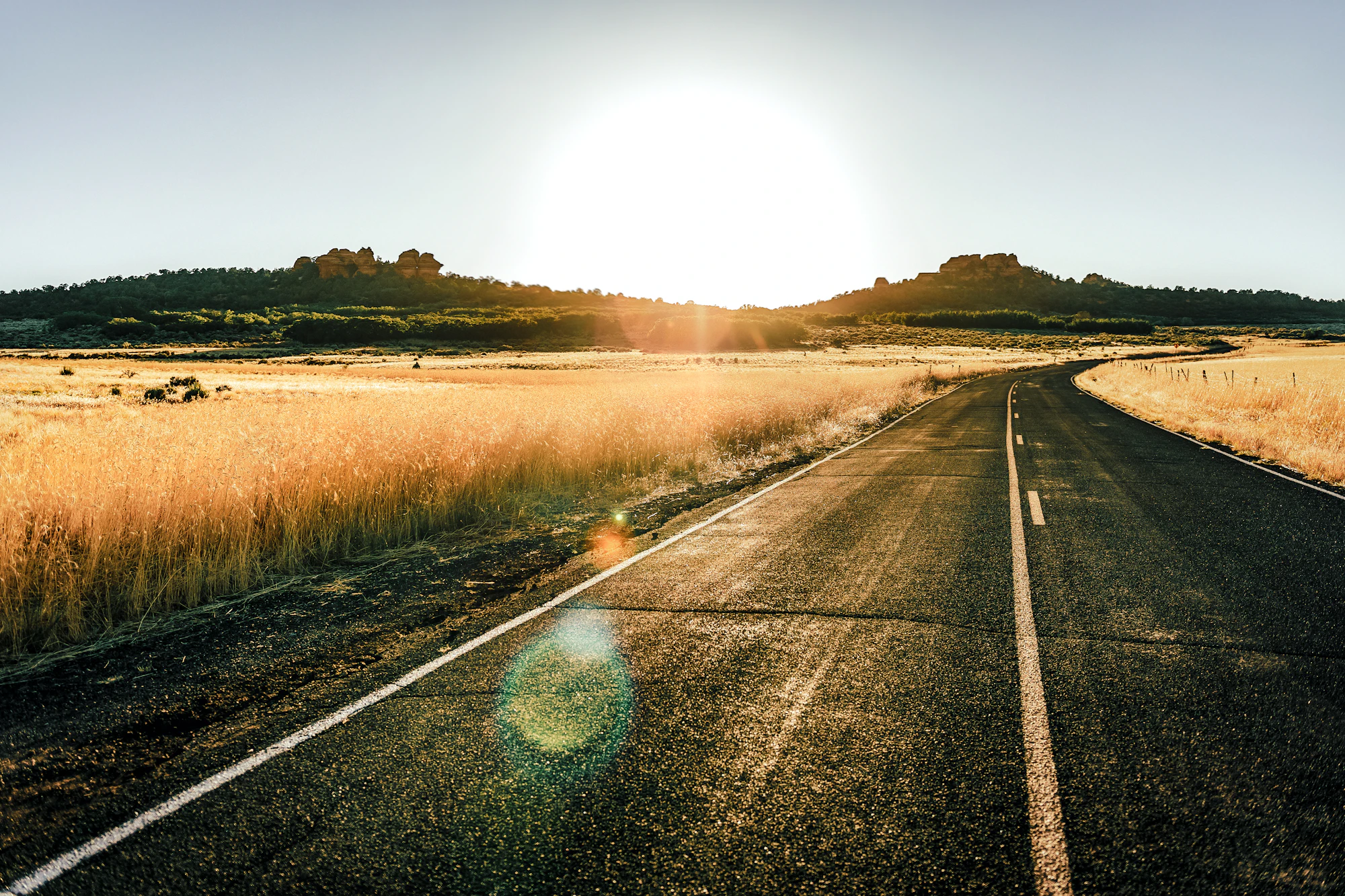 Open road leading toward sunlit hills at sunrise