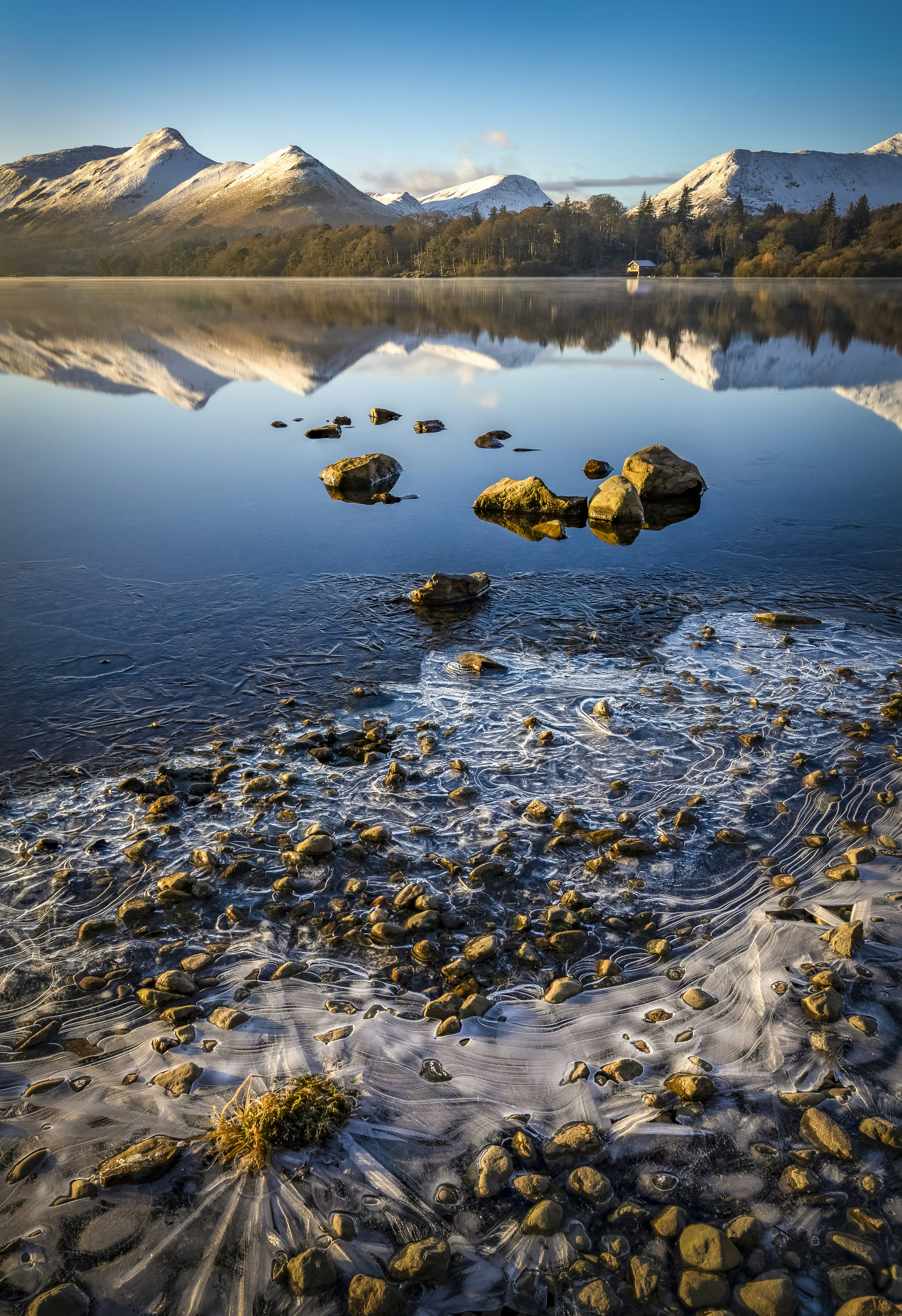 Montanhas nevadas refletidas em um lago calmo com costa gelada.