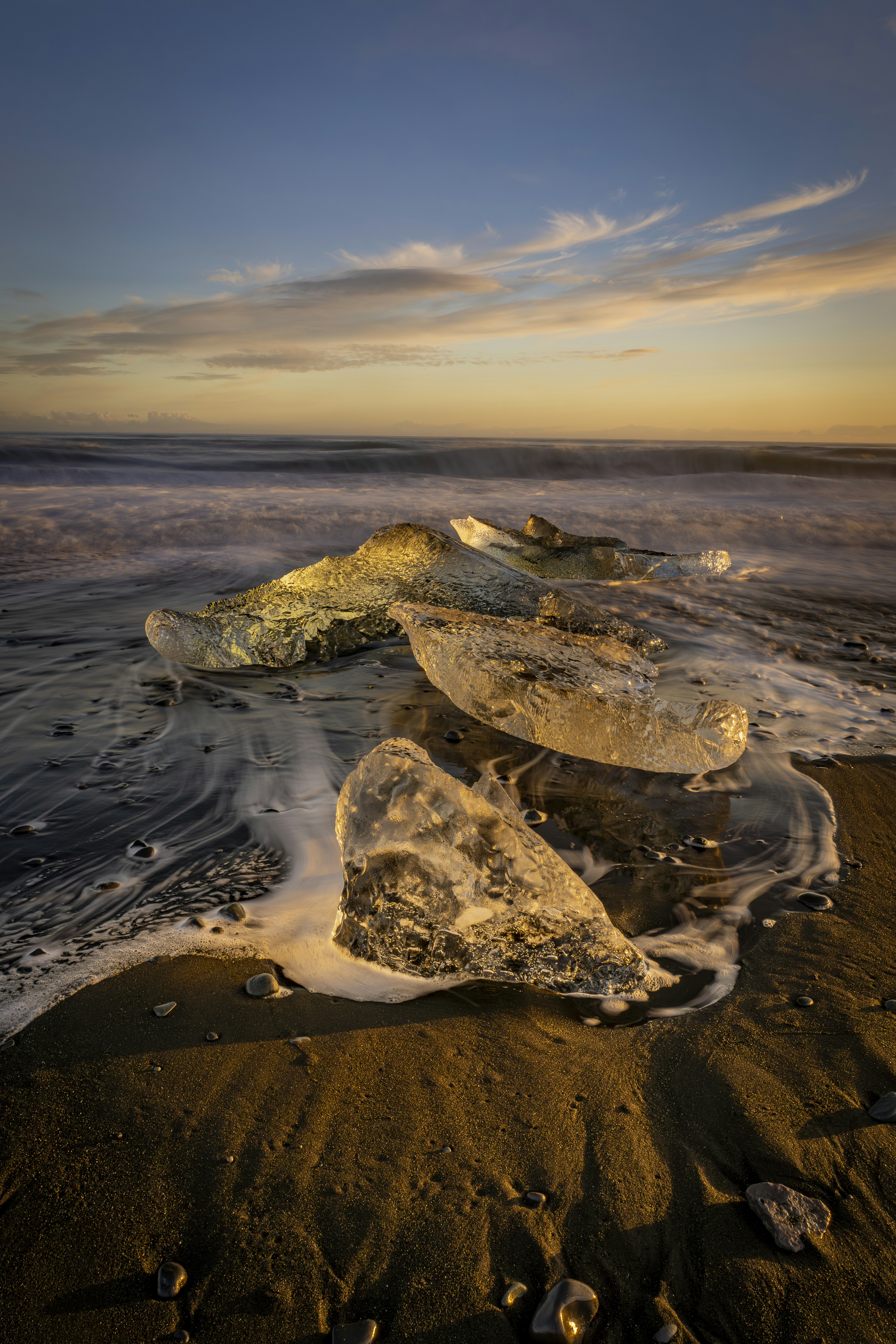 Ice chunks on a sandy beach at sunset.