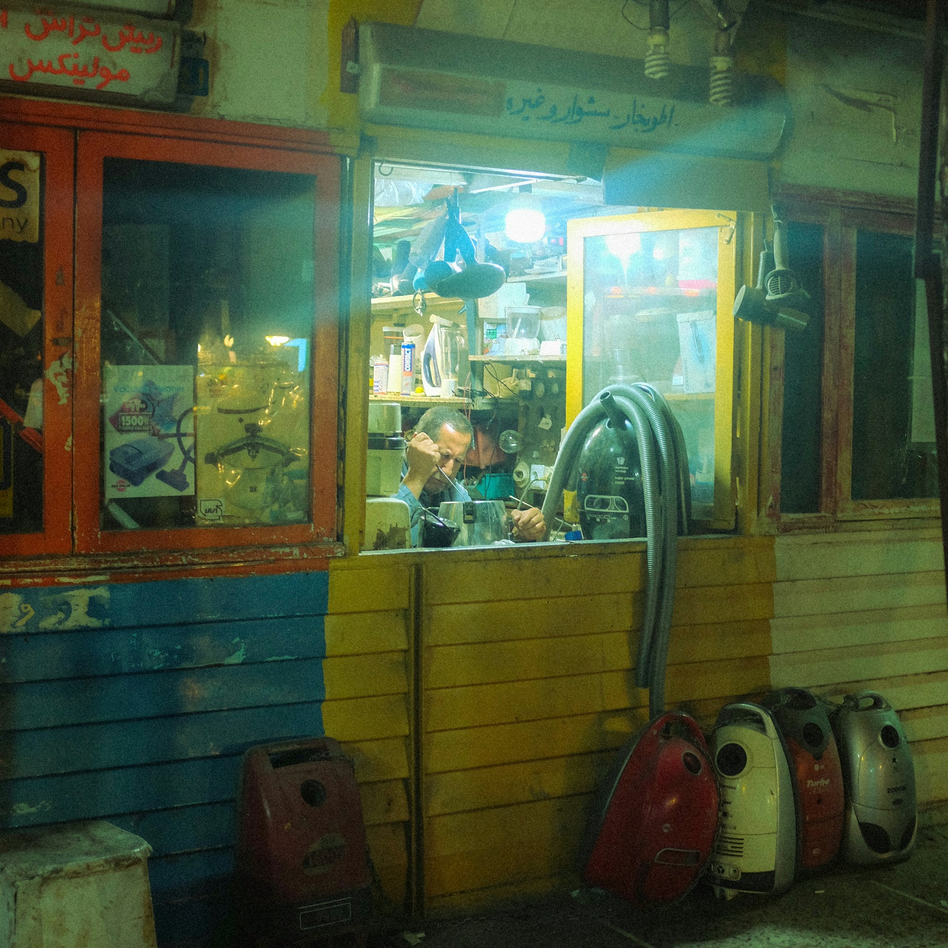 Man working in a colorful shop with vacuum cleaners outside.