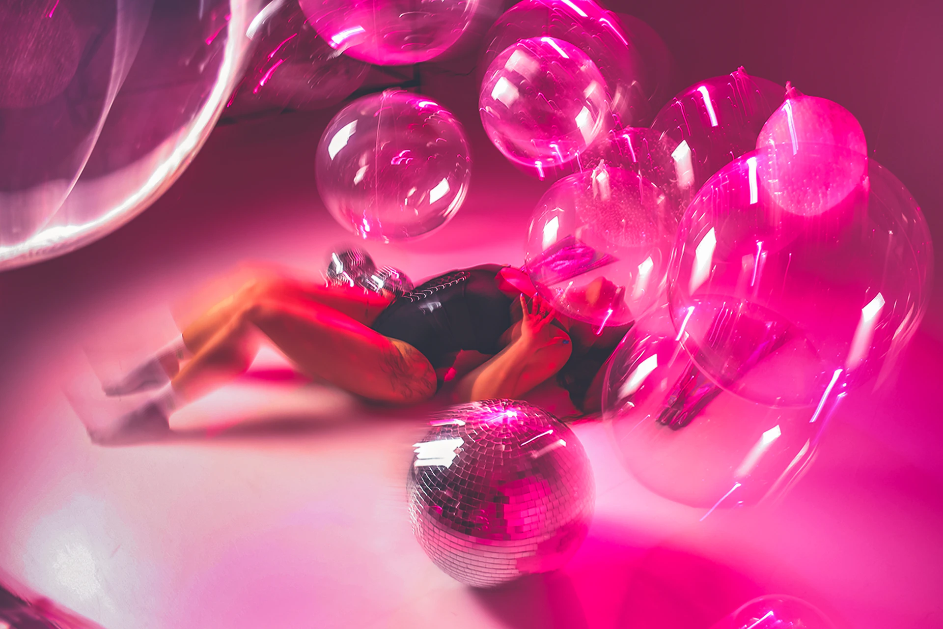 Woman lying down surrounded by pink bubbles and disco ball.