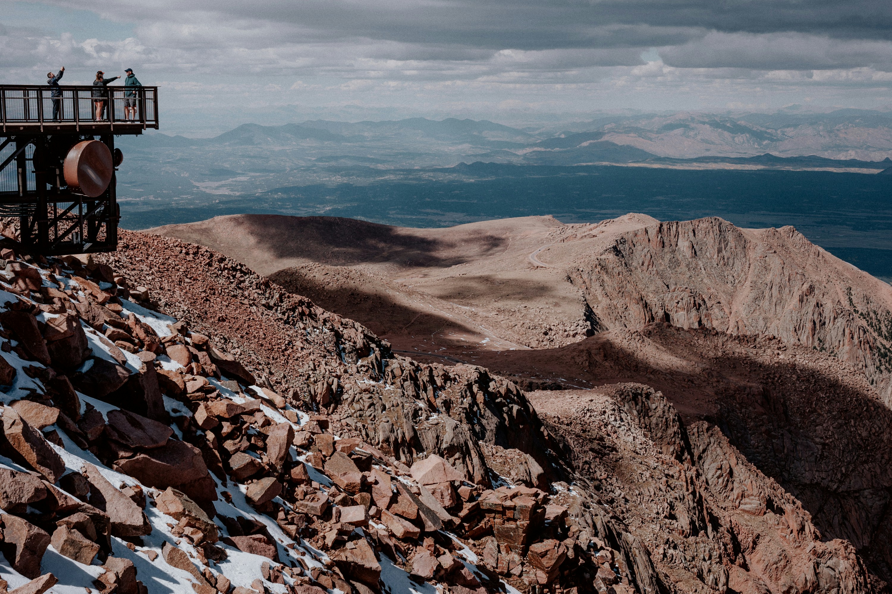 People on a scenic overlook above rocky mountains.