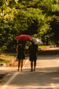 Two people walk with umbrellas on a sunny day.