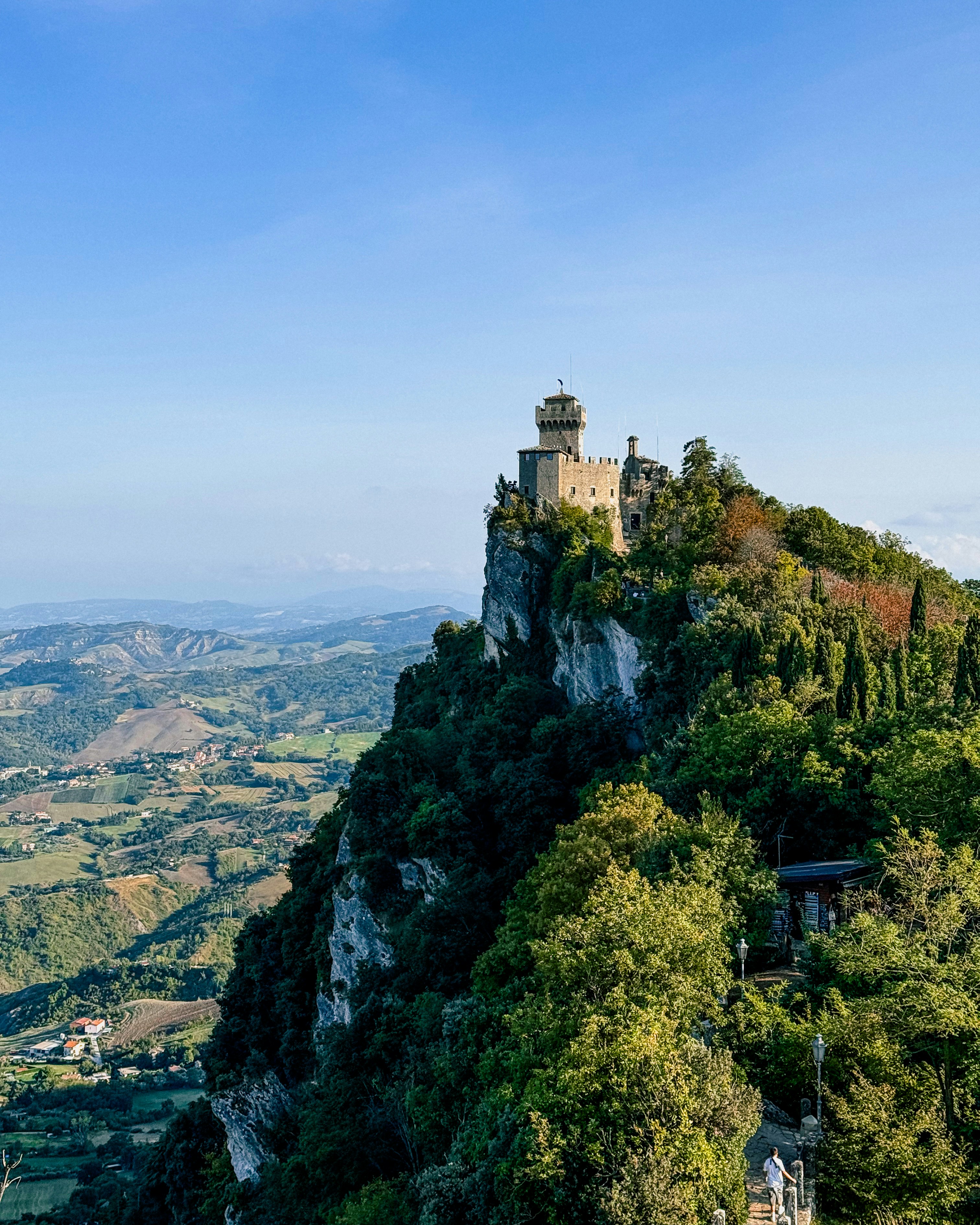 Castle perched on a rocky cliff overlooking green hills.