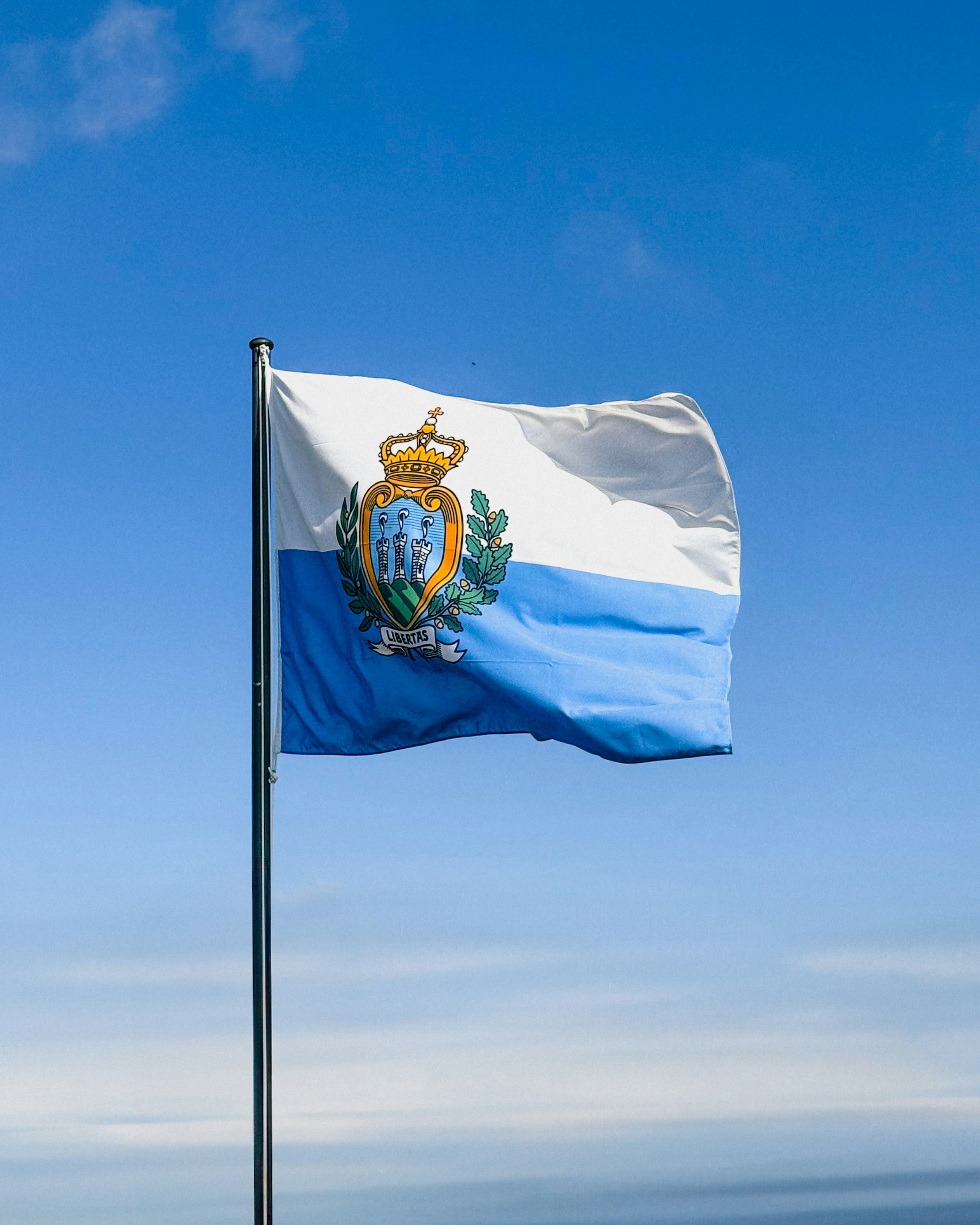 The flag of san marino waves against a blue sky.