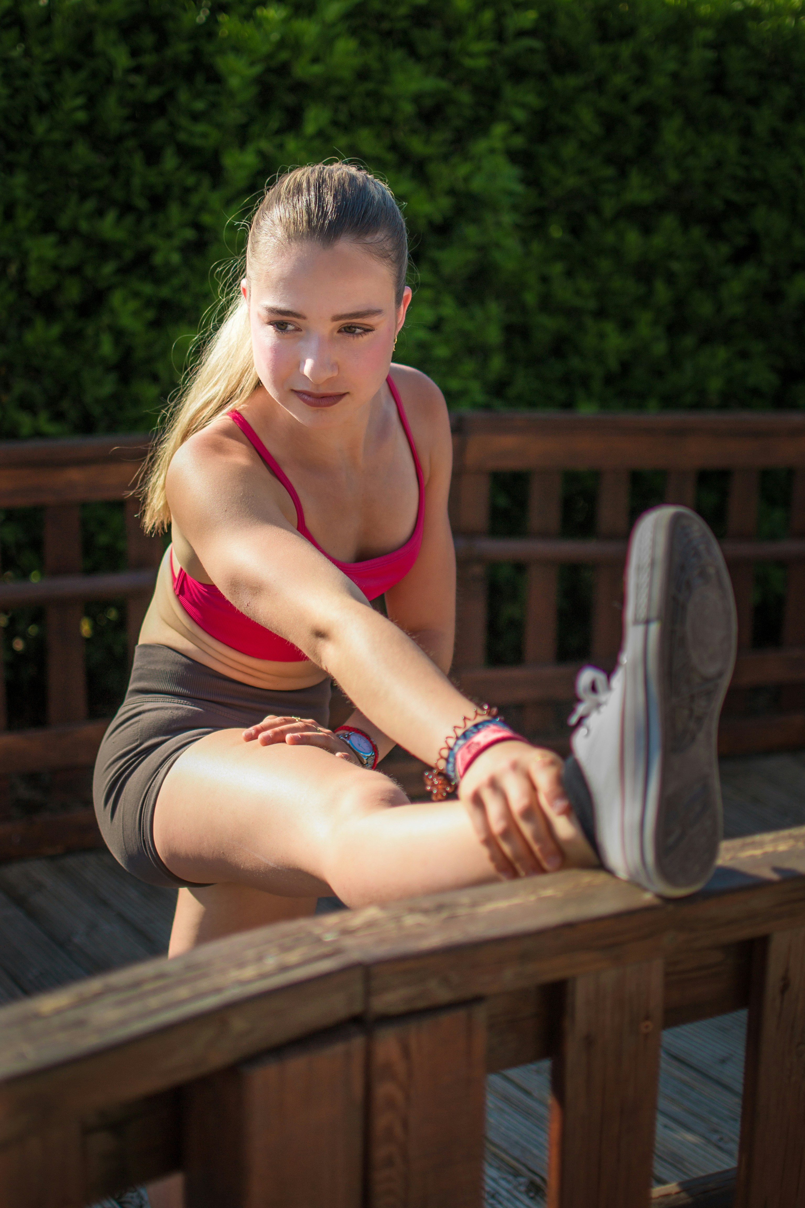 Young woman stretching her leg outdoors on a wooden deck.