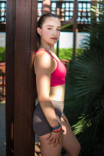 Young woman in athletic wear leans against wooden post.