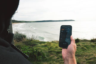 Person holding phone overlooking ocean and beach