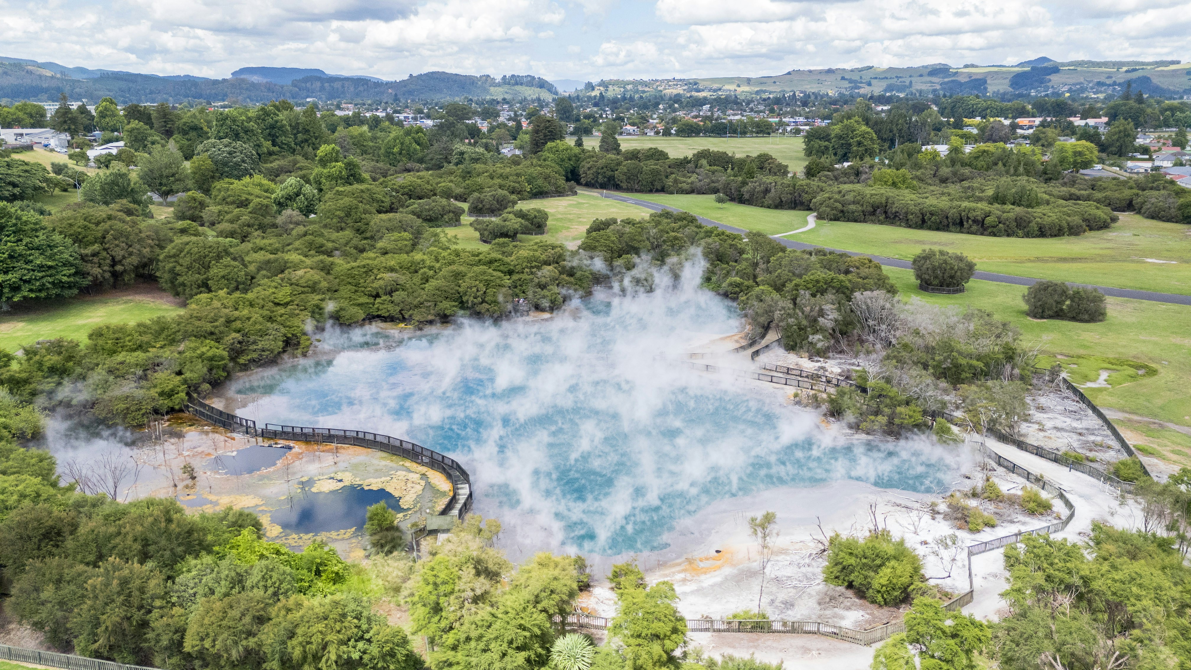 Dampfender geothermischer Pool, umgeben von üppigen grünen Bäumen