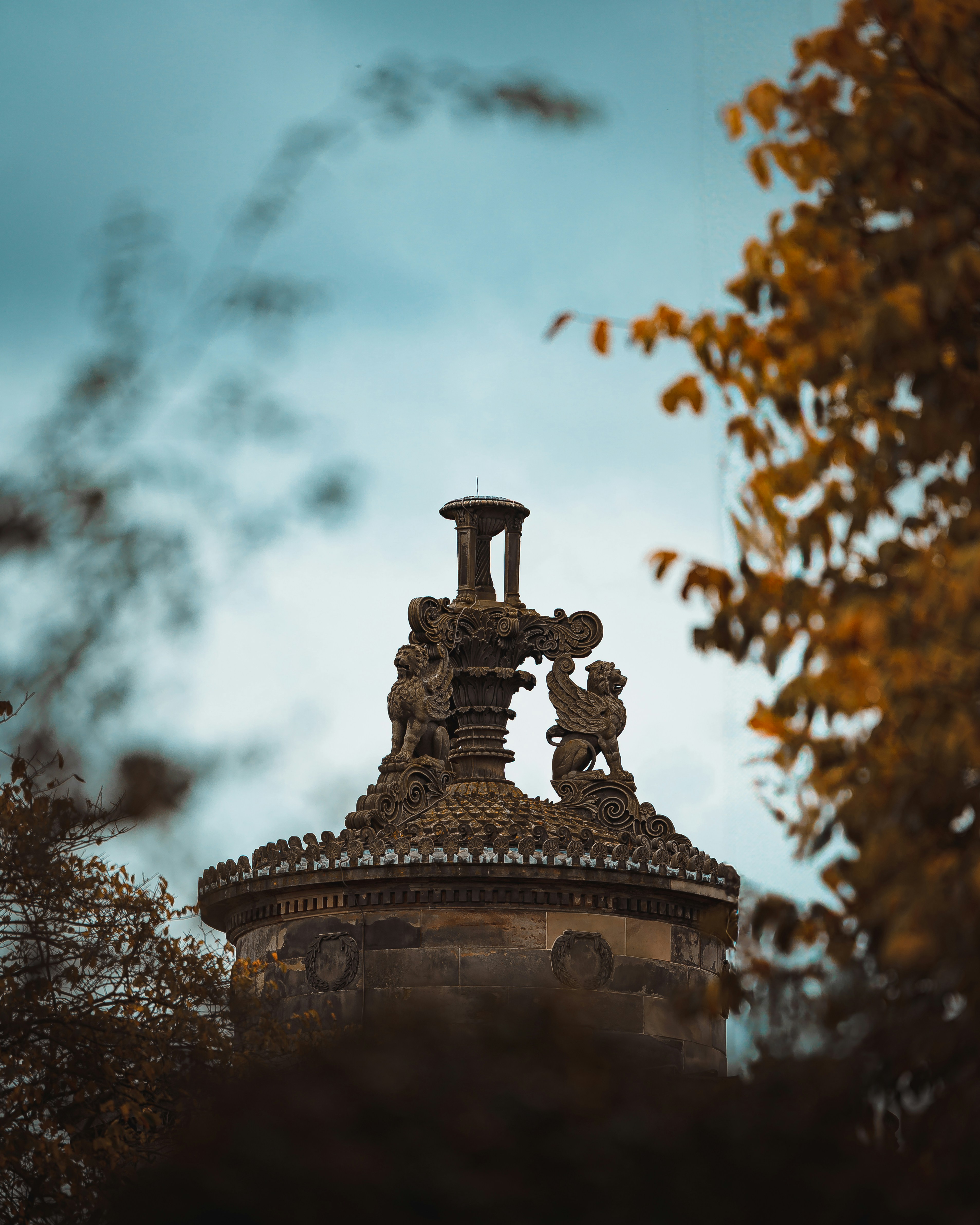 Ornate stone monument with animal carvings framed by trees.
