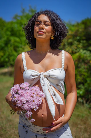 Pregnant woman holding pink flowers with eyes closed
