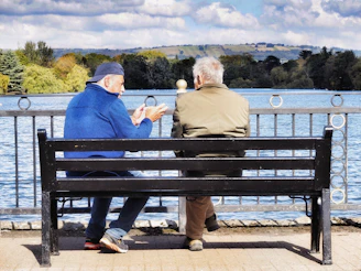 Two men sit on a bench by the water