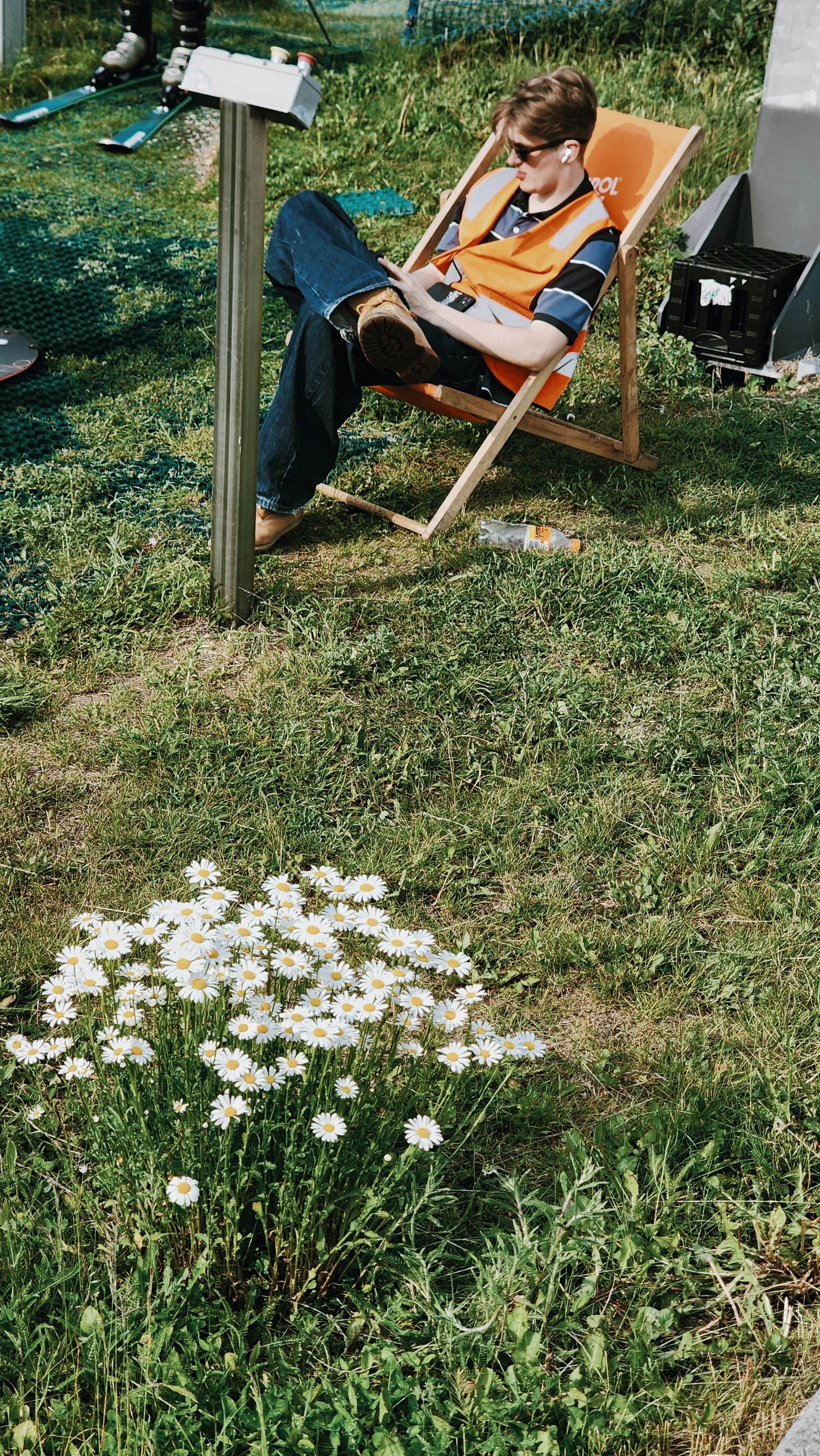 Man in orange vest relaxes in deck chair near daisies.