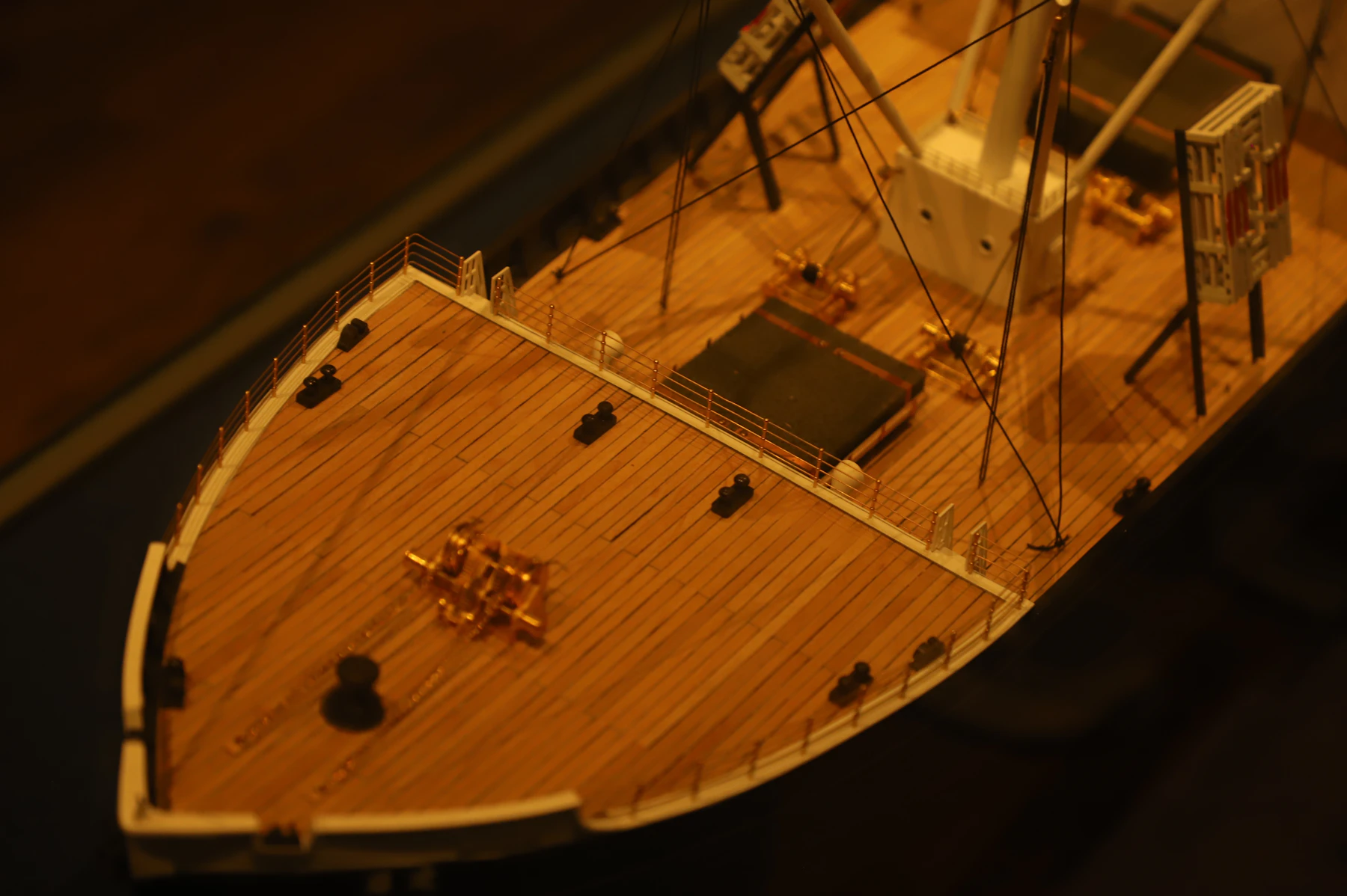 The planked wooden deck of a model ship seen from above the bow, with railings and deck fittings