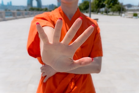 Person in orange shirt holds up hand