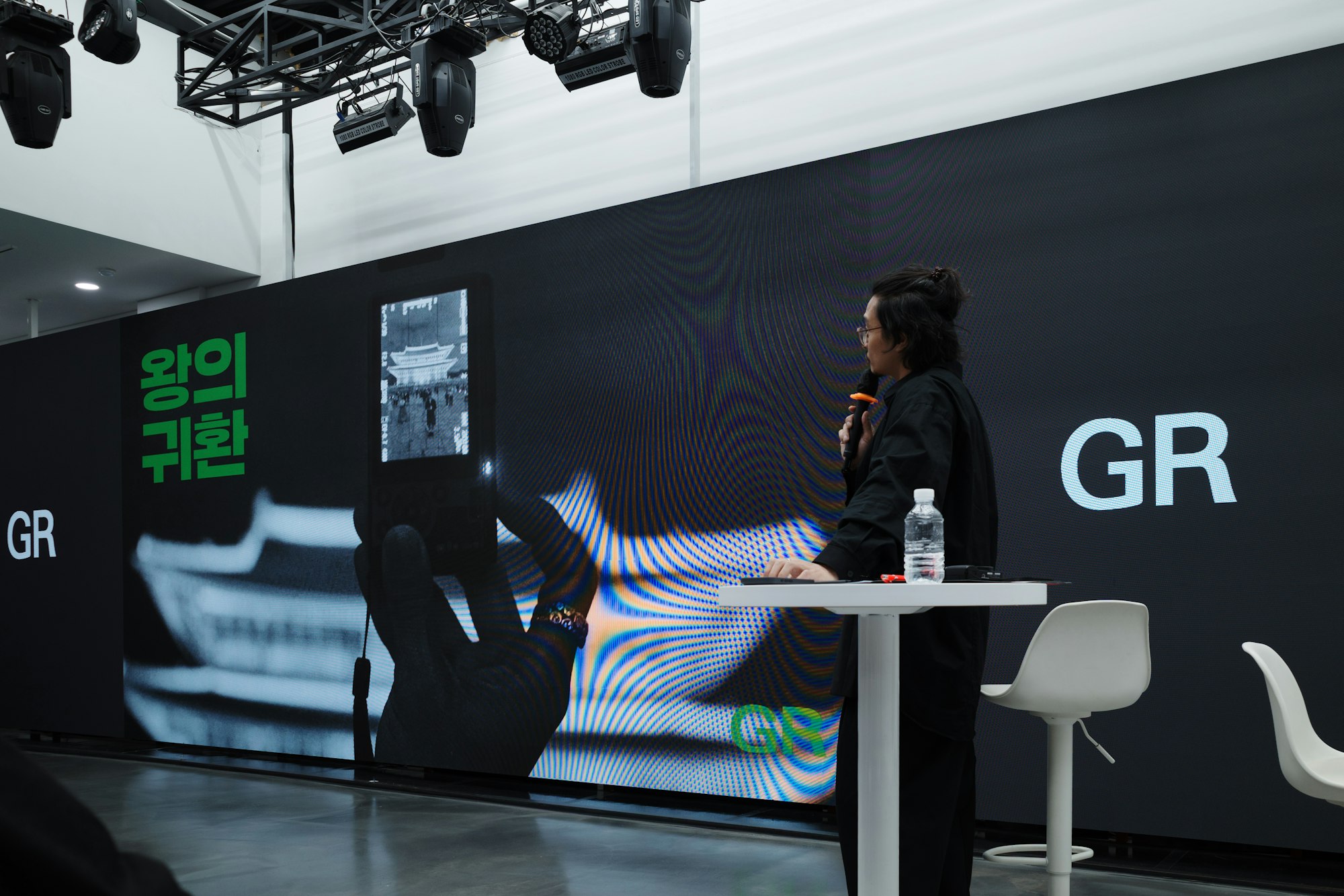A speaker presents at a conference event with a large screen display behind them