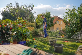 Man walks through a lush garden with a house.