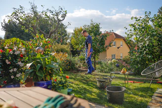 Man walks through a lush garden with a house.