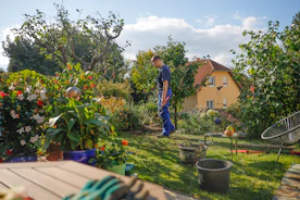Man walks through a lush garden with a house.