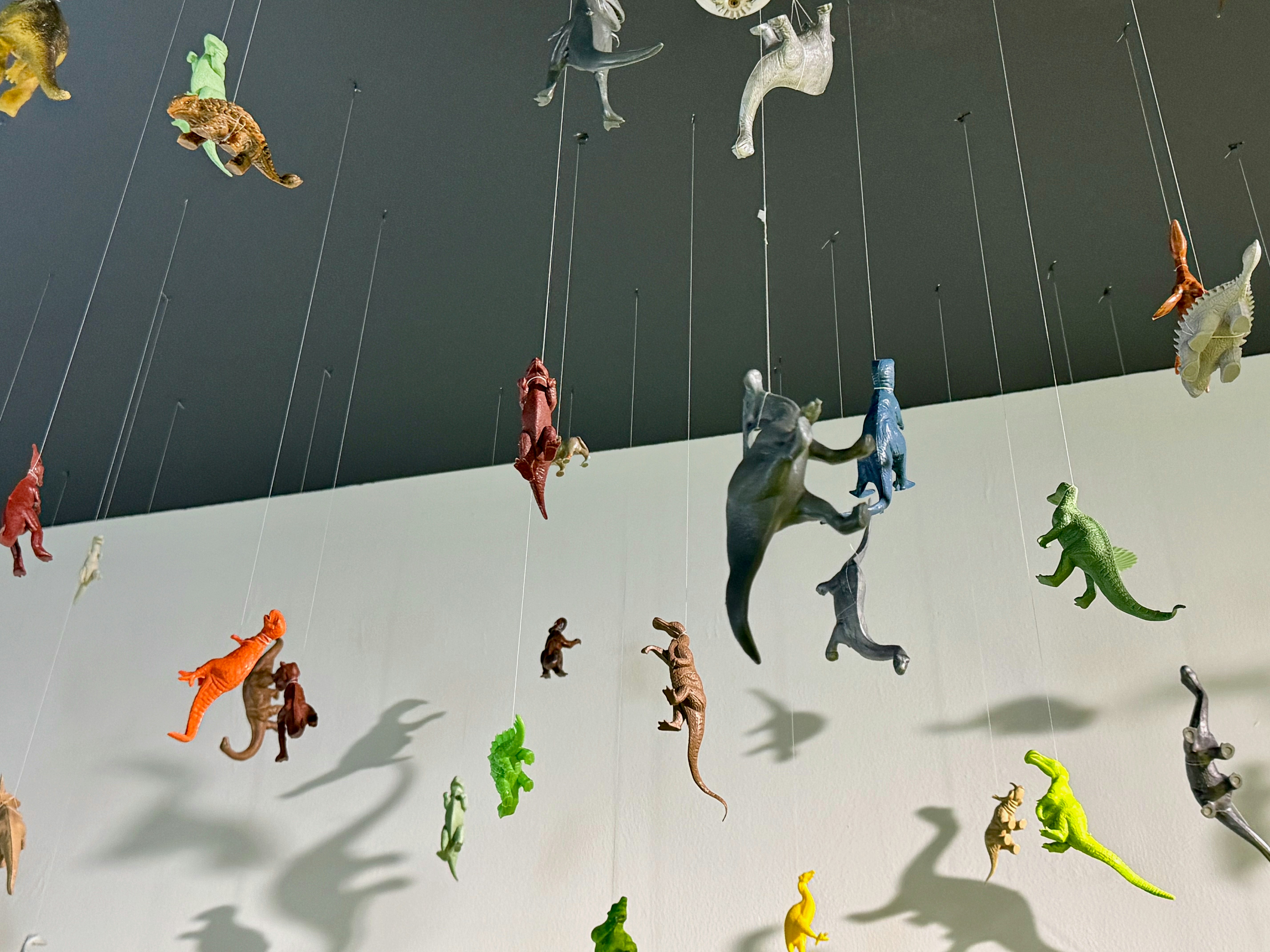 Toy dinosaurs suspended from strings against a wall.