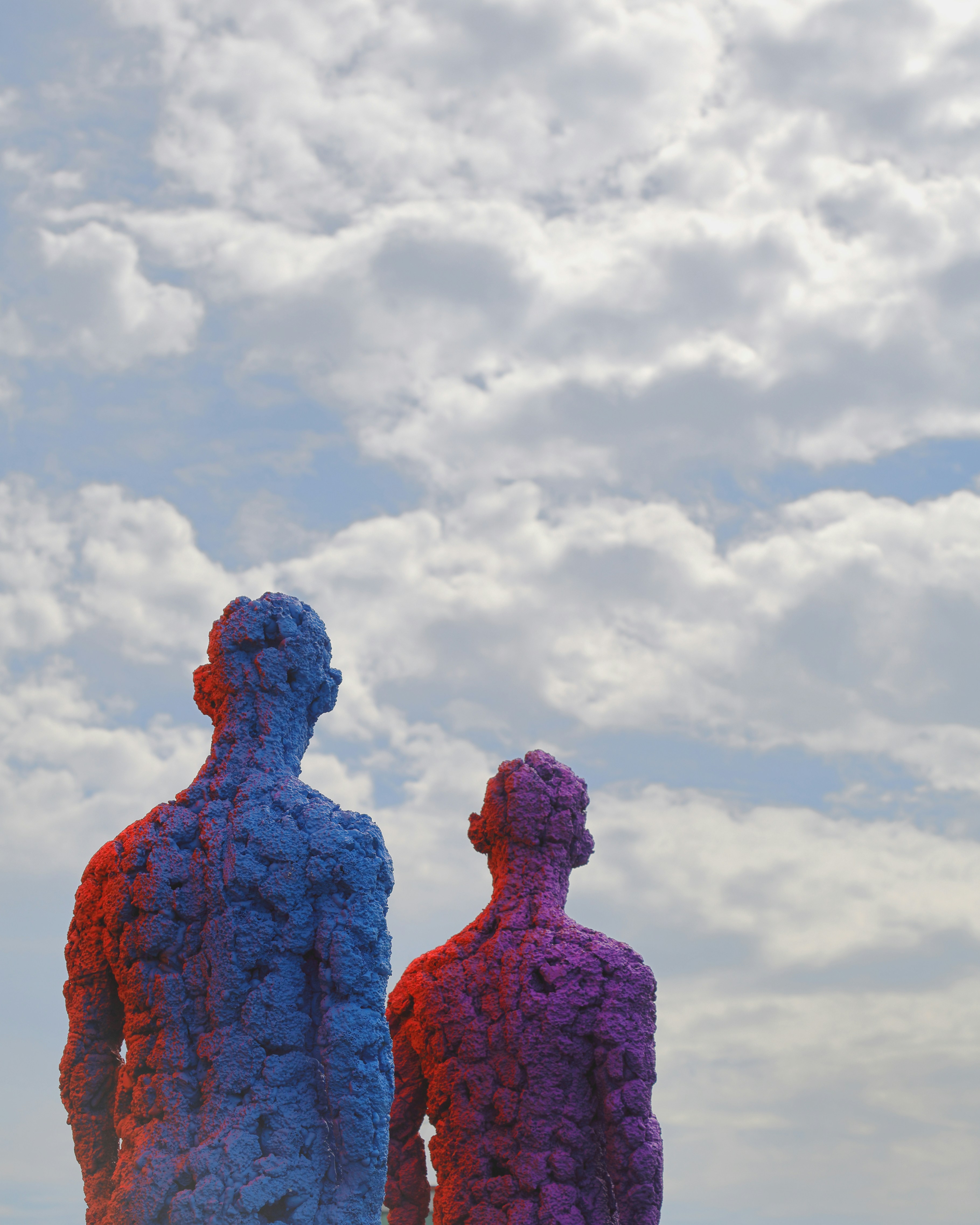 Two textured figures against a cloudy sky