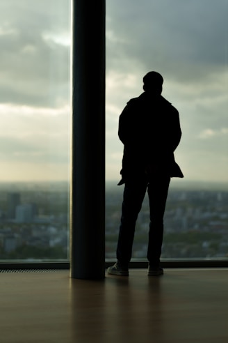 Man stands silhouetted against city view window.