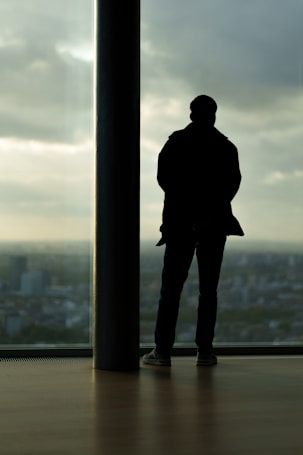 Man stands silhouetted against city view window.