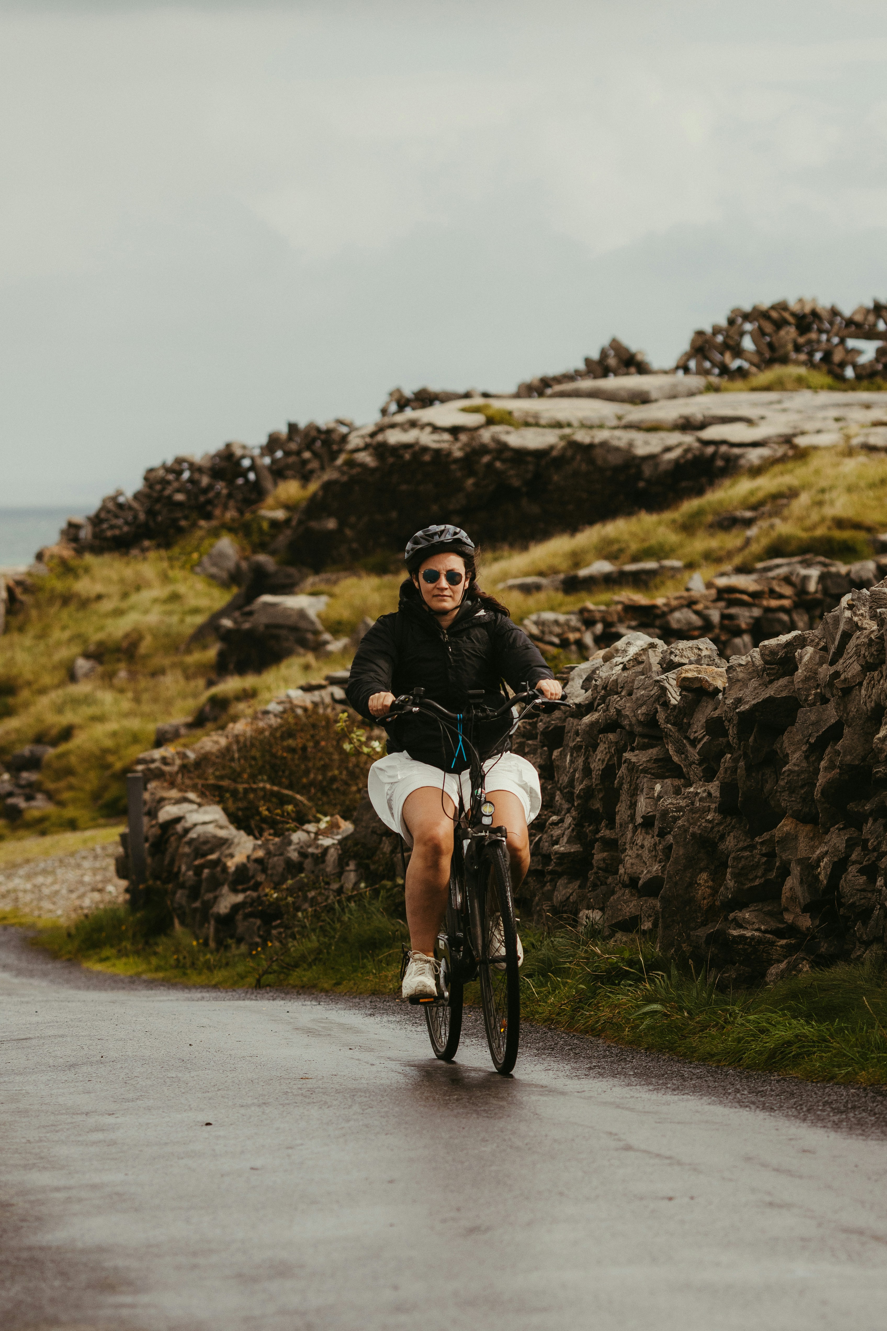 Woman cycling on a wet road near stone walls