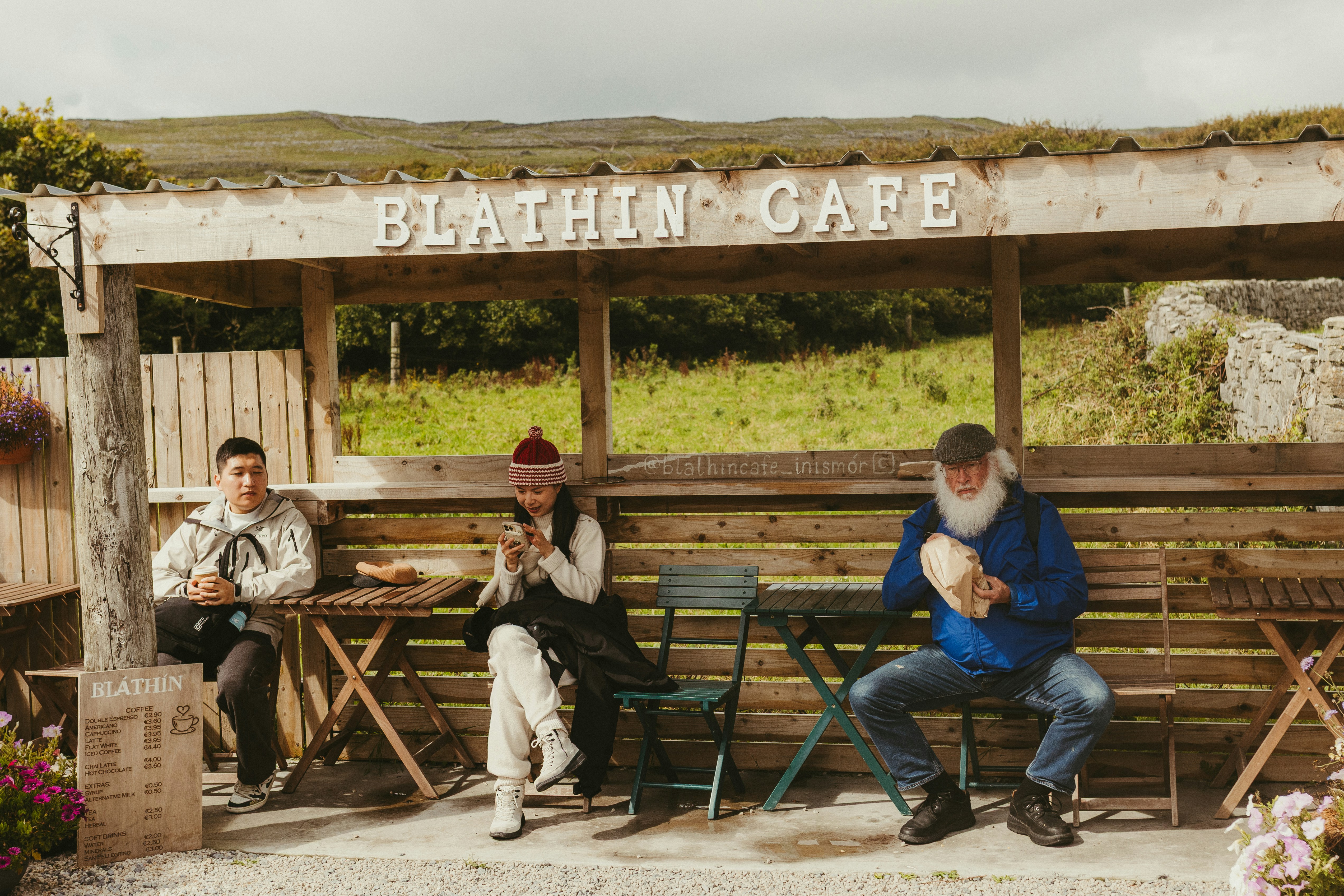 Three people sitting outside a cafe with mountains behind.