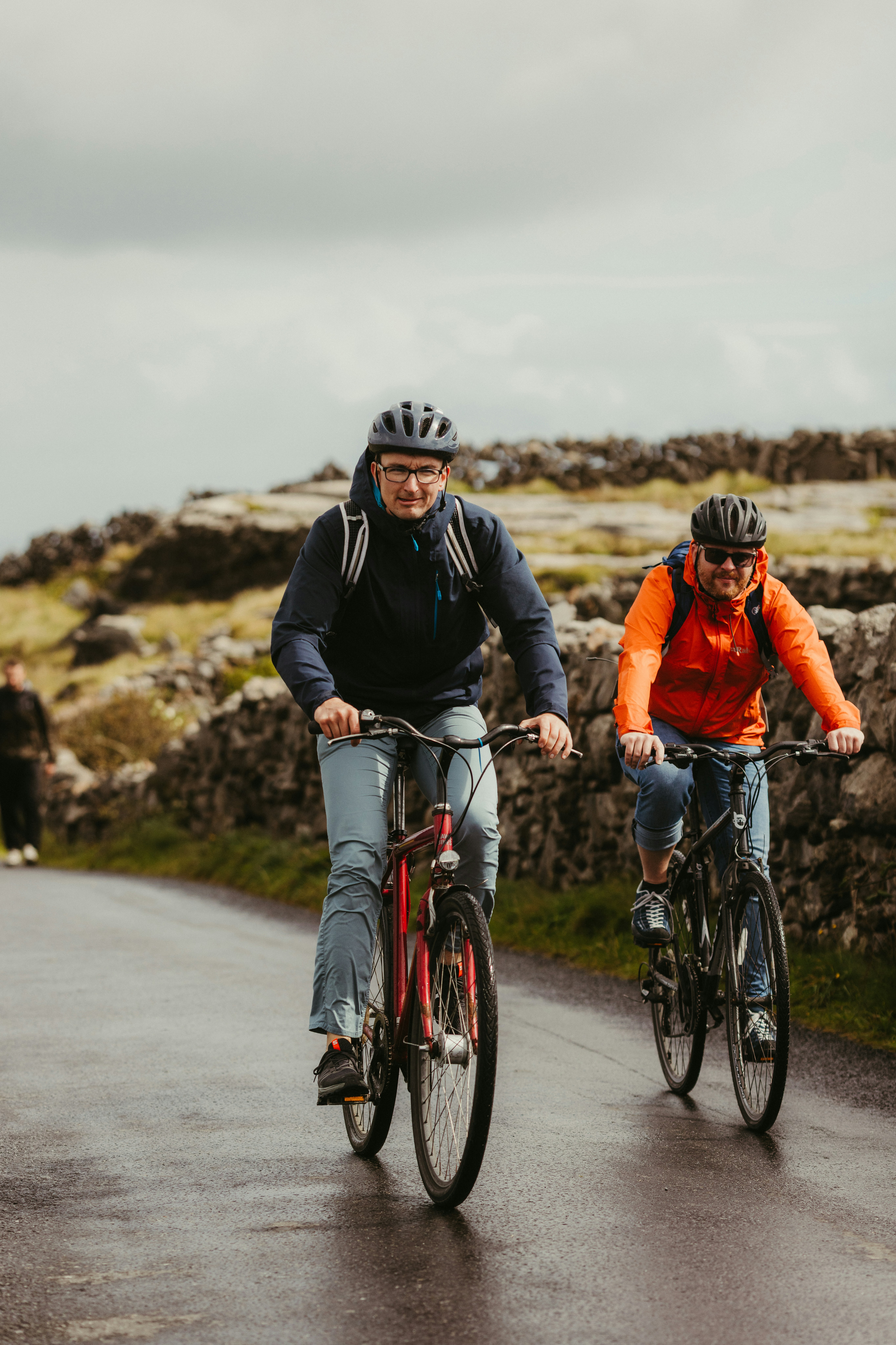 Two people cycling on a wet road with stone walls.