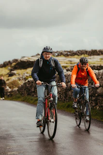 Two people cycling on a wet road with stone walls.