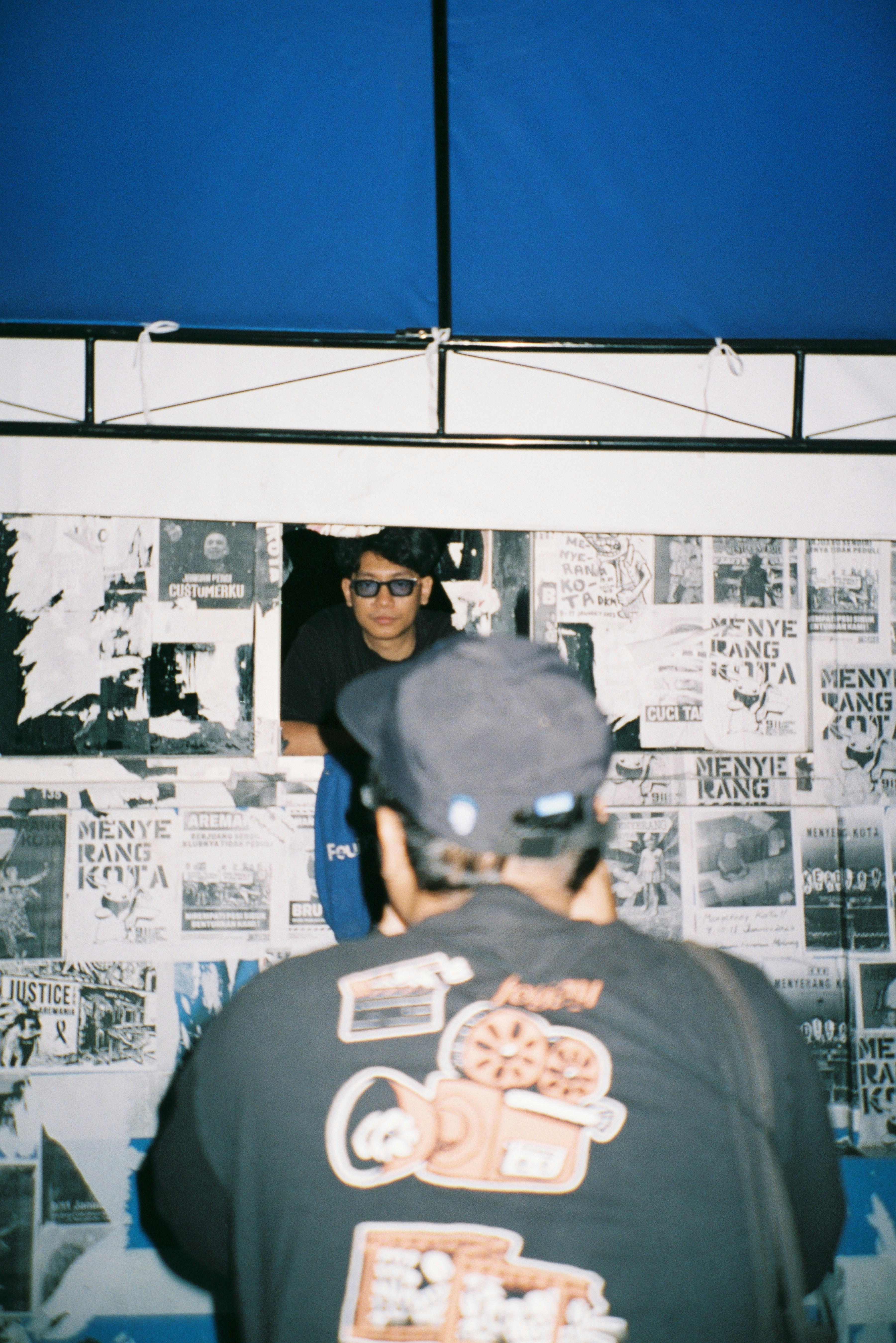 Two people at a booth with posters on wall.