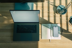 Laptop, phone, and notebook on a wooden desk.